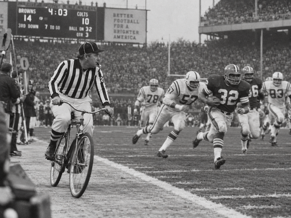 A referee pedals a bicycle down the sideline to keep up with the play.