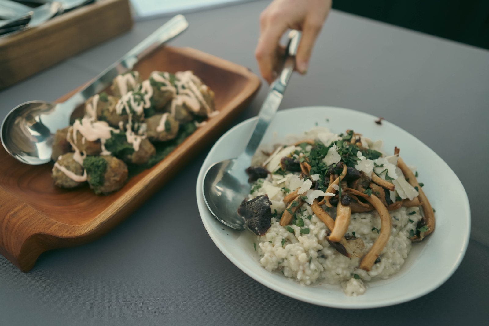 A plate of mushroom risotto beside a wooden board of appetizers on a gala table.