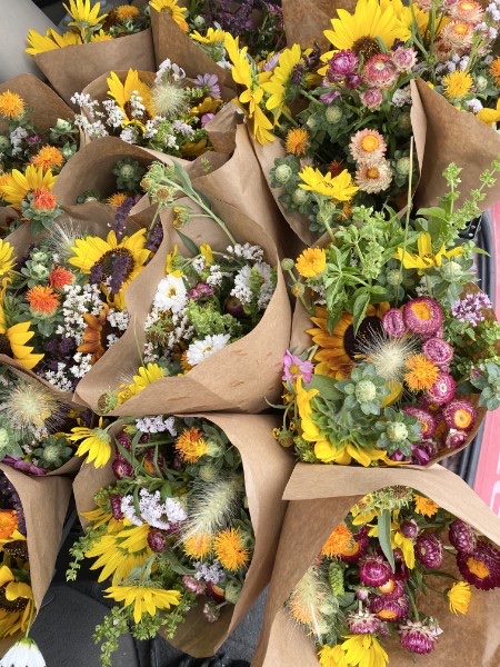 Bouquets of sunflowers, zinnias, and strawflowers wrapped in kraft paper.