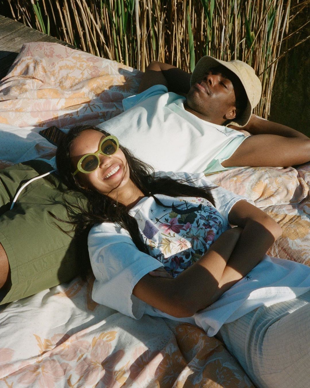 Two young women lying on grass, one smiling with eyes closed, the other relaxed with eyes closed.