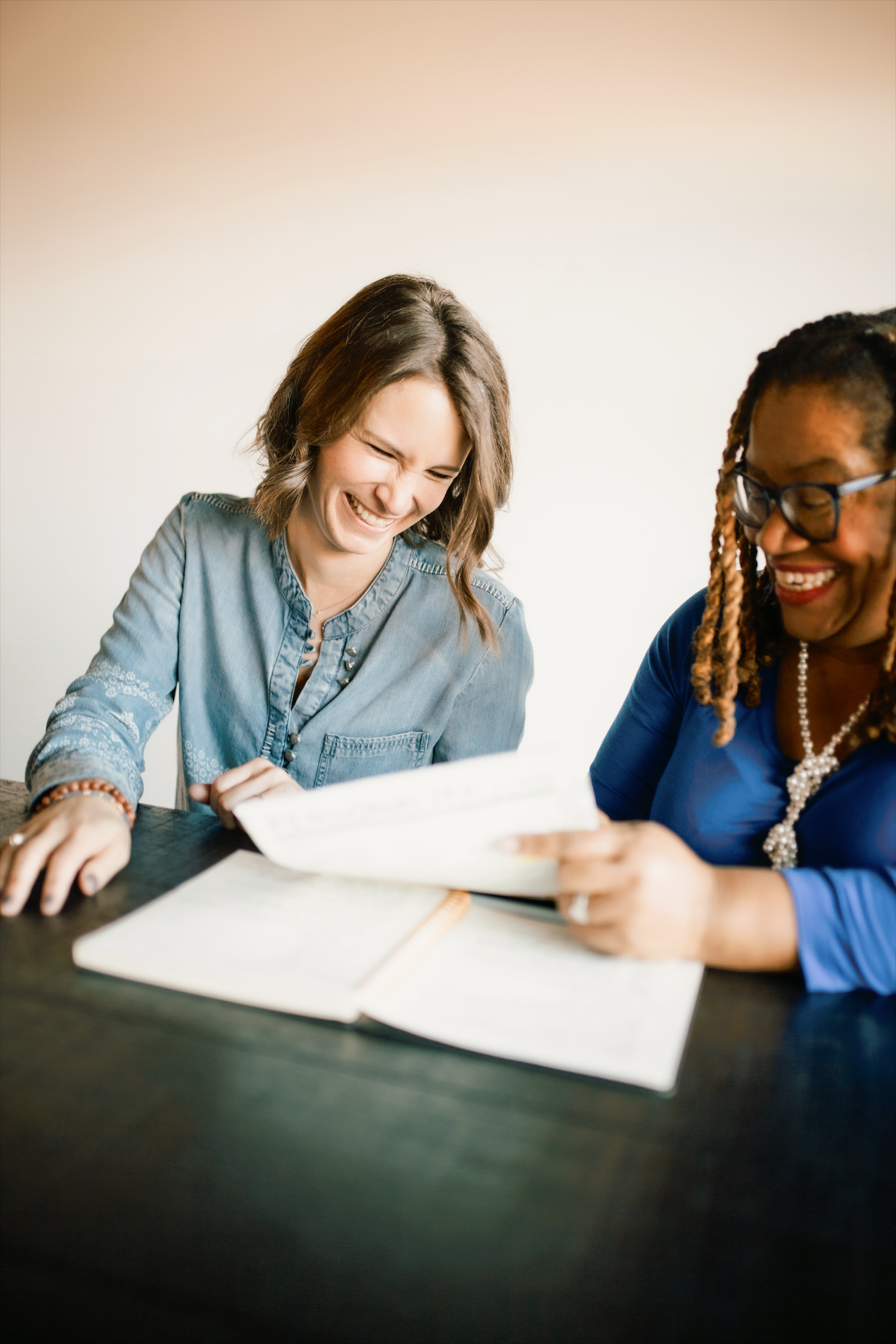 Young girl using a laptop with an adult woman helping her from behind at a wooden table.