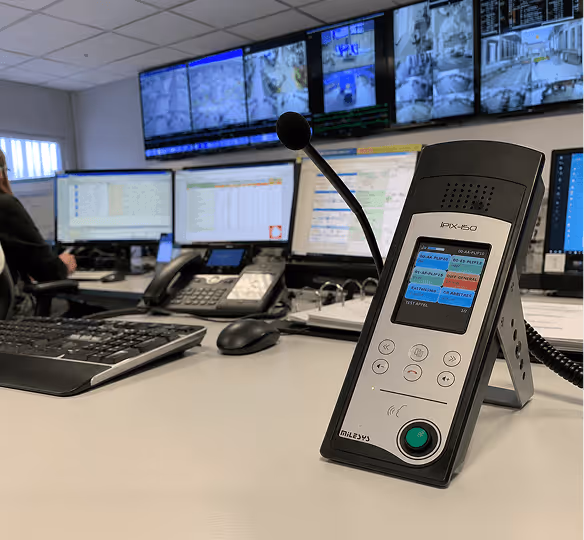 Microphone de bureau IPX-50 avec écrans de surveillance et claviers dans la salle de contrôle.