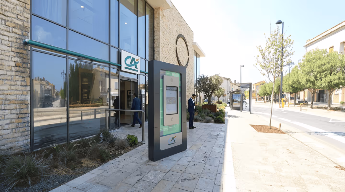 Façade d'une banque avec homme en costume entrant et autre utilisant son téléphone dehors.