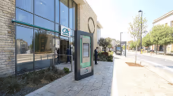 Arrêt de bus avec panneau publicitaire près d'un bâtiment avec vitres sur une rue ensoleillée.