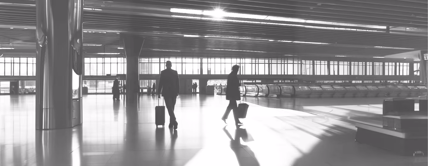 Deux voyageurs avec des bagages dans un hall d'aéroport large et lumineux au sol réfléchissant.