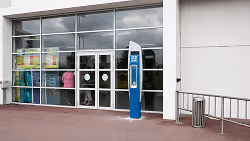 Façade d'un bâtiment avec grande vitrine, porte en verre et borne de commande bleue devant.