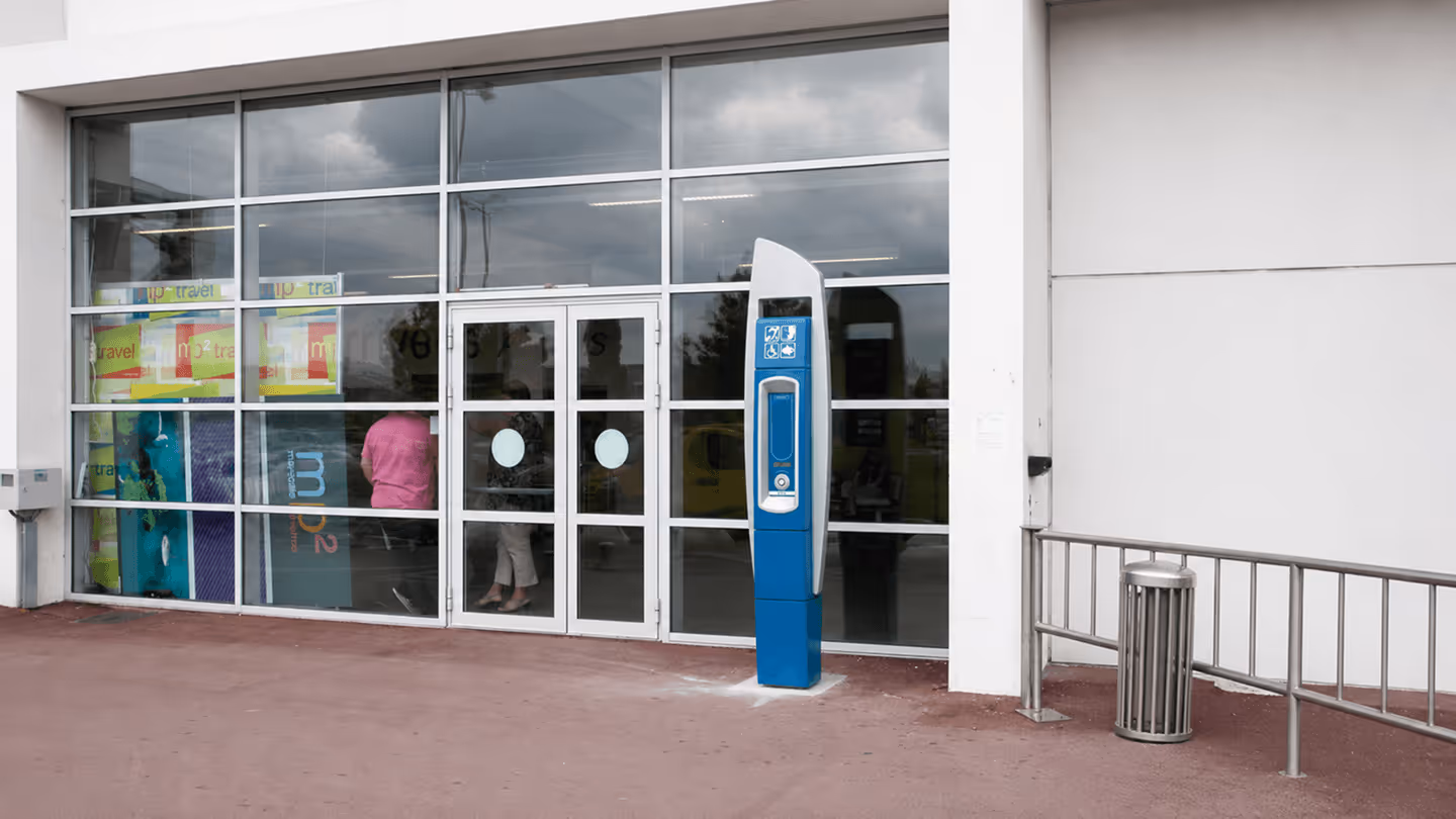 Borne de recharge bleue pour véhicule électrique devant une entrée vitrée d’un bâtiment.