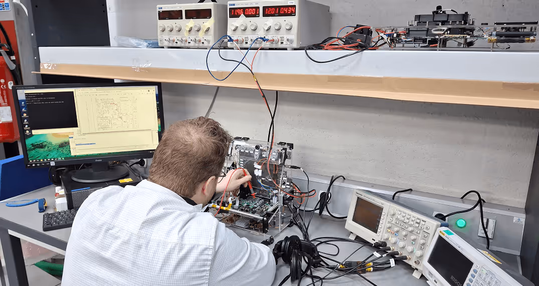 Appareil Thales posé sur une surface blanche avec un fond de panneaux verts en forme de pyramides.