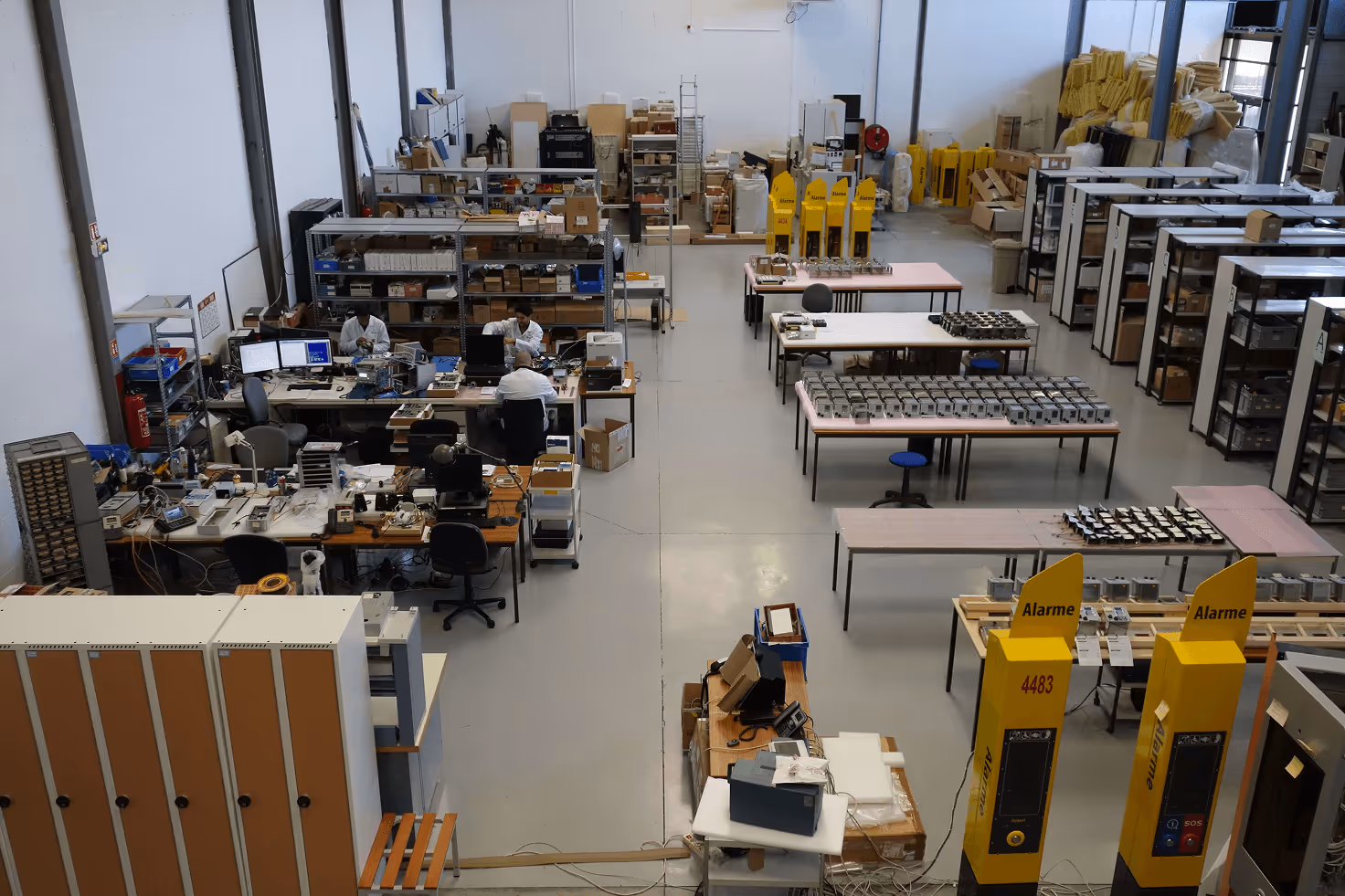 Vue d'atelier de production avec bureaux, tables et équipements électroniques organisés.