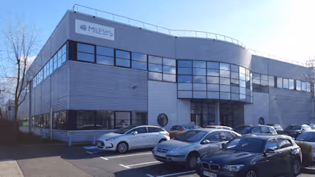 Bâtiment d’entreprise moderne avec des voitures stationnées devant sous un ciel bleu clair.