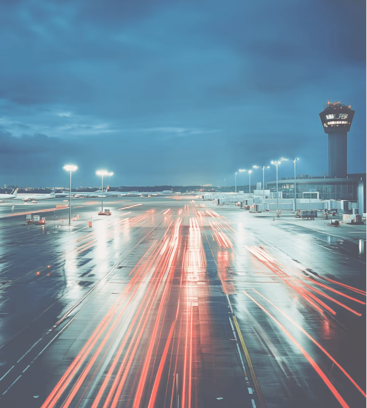 Piste d'aéroport la nuit avec traînées lumineuses rouges et bâtiment de contrôle aérien éclairé.