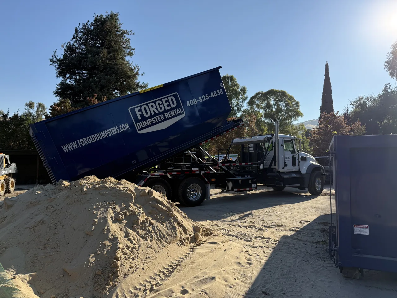 Forged roll off truck tipping a branded dumpster at a job site