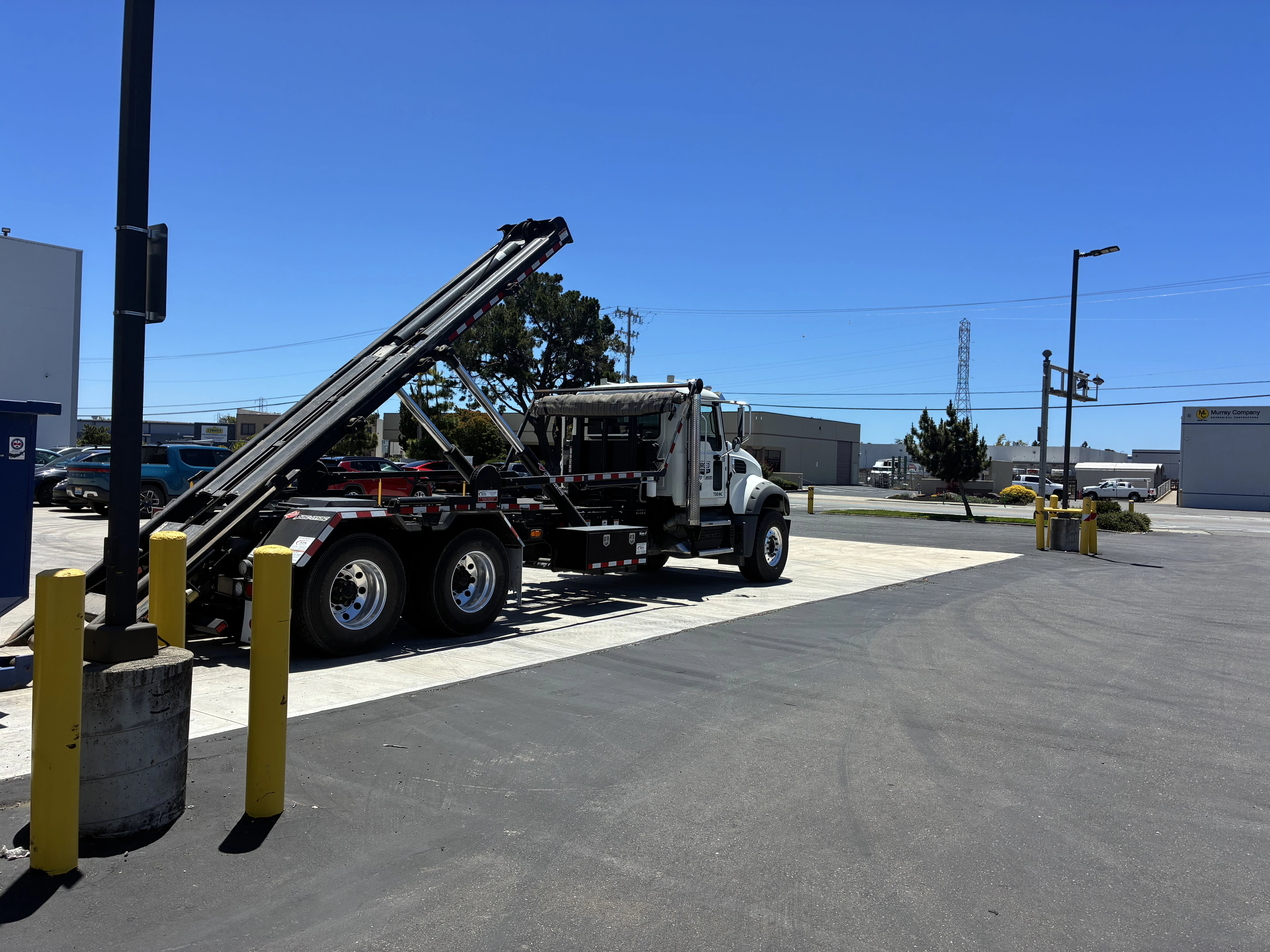 Roll-off truck with raised arms at an industrial lot