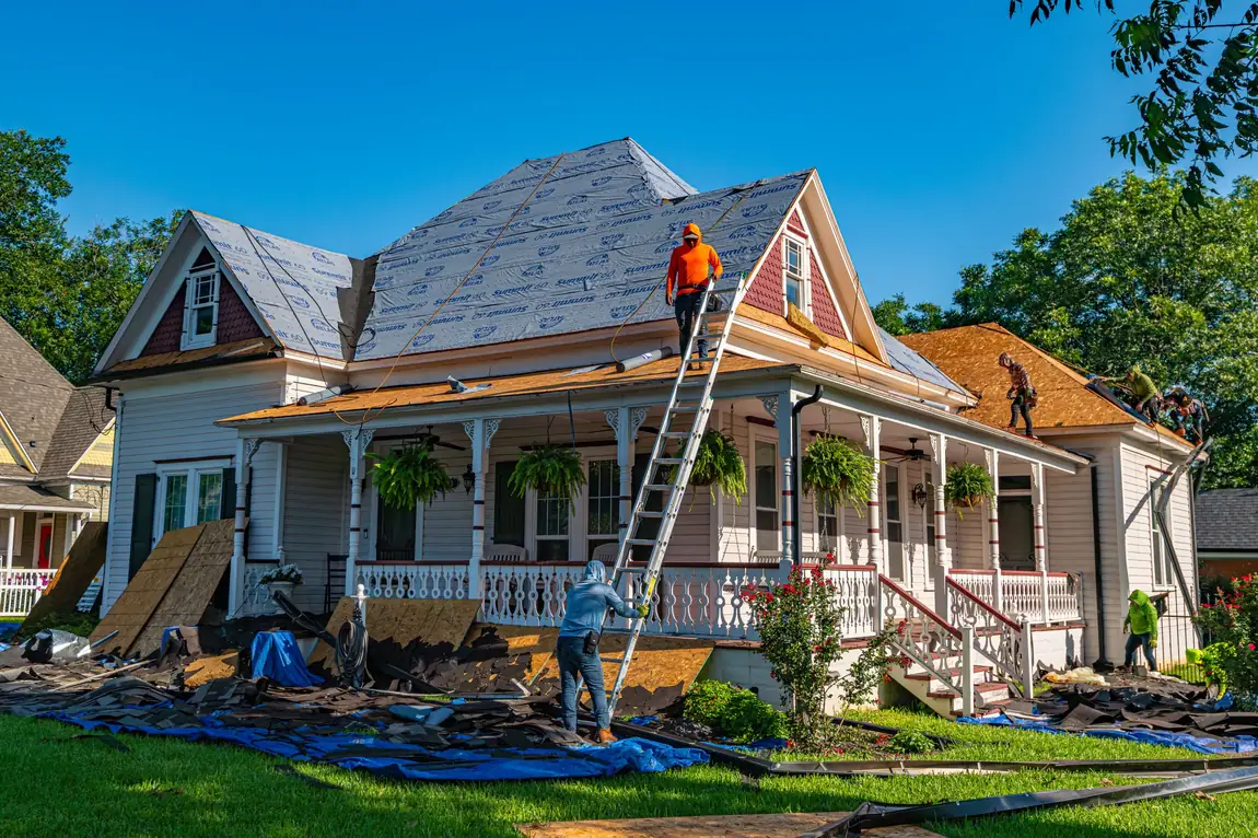 Victorian home mid roof replacement with torn-off shingles piled on tarps across the front lawn