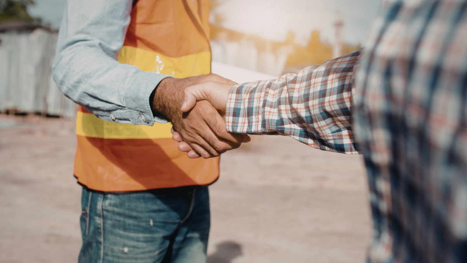Contractor in an orange safety vest shaking hands with a client on a sunny job site