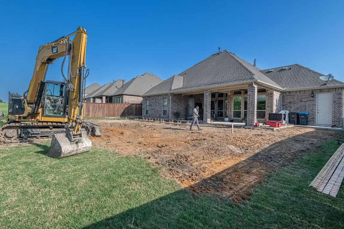 Compact excavator regrading a suburban backyard patio during a home project that generates heavy debris