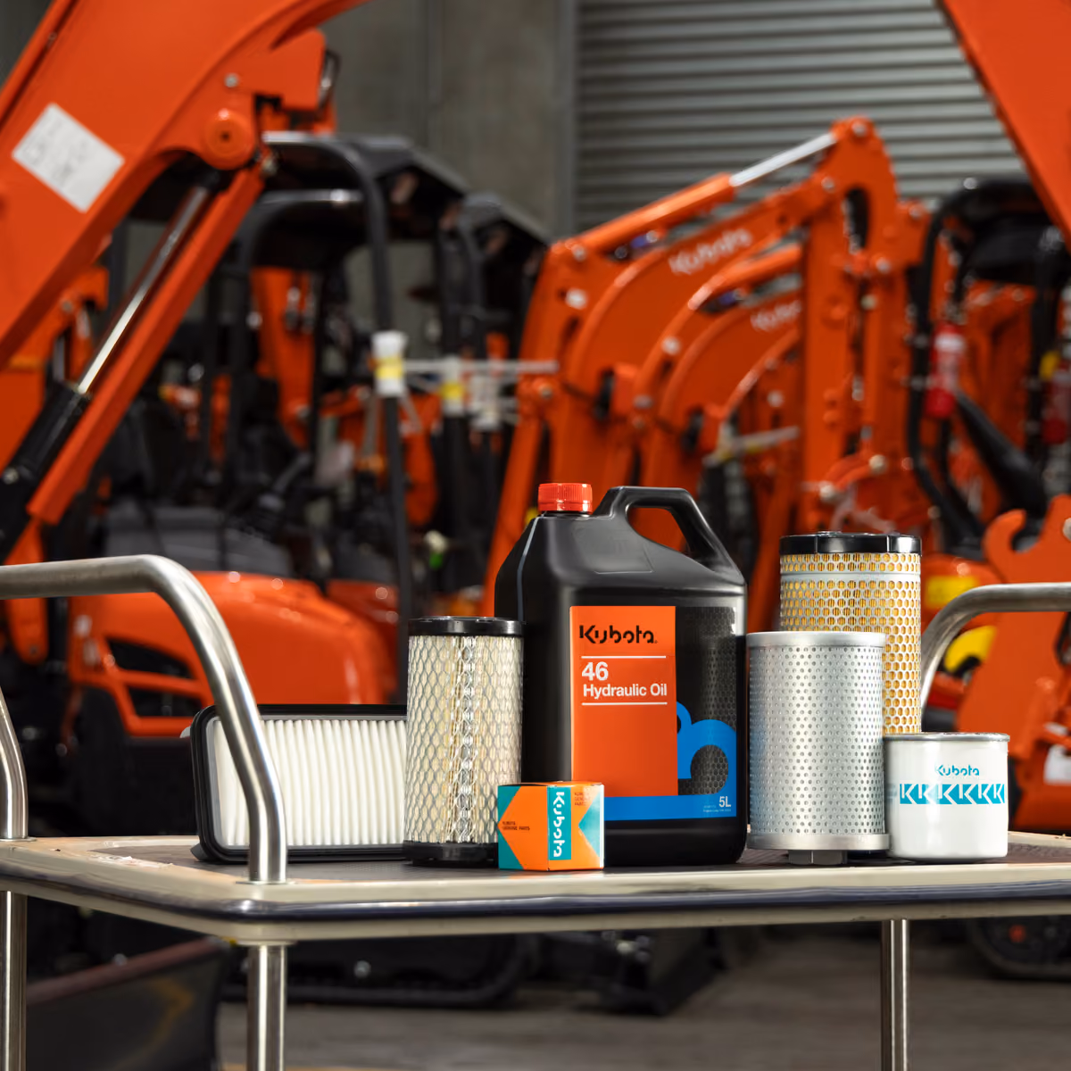 Kubota filters and hydraulic oil on a workshop trolley in front of tractors and excavators.