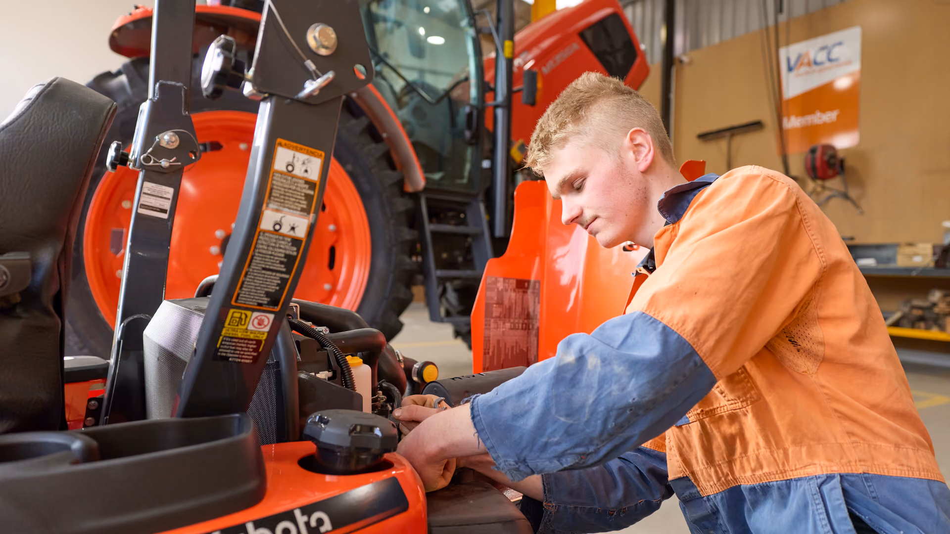 Technician in hi-vis servicing an orange Kubota machine in the workshop.