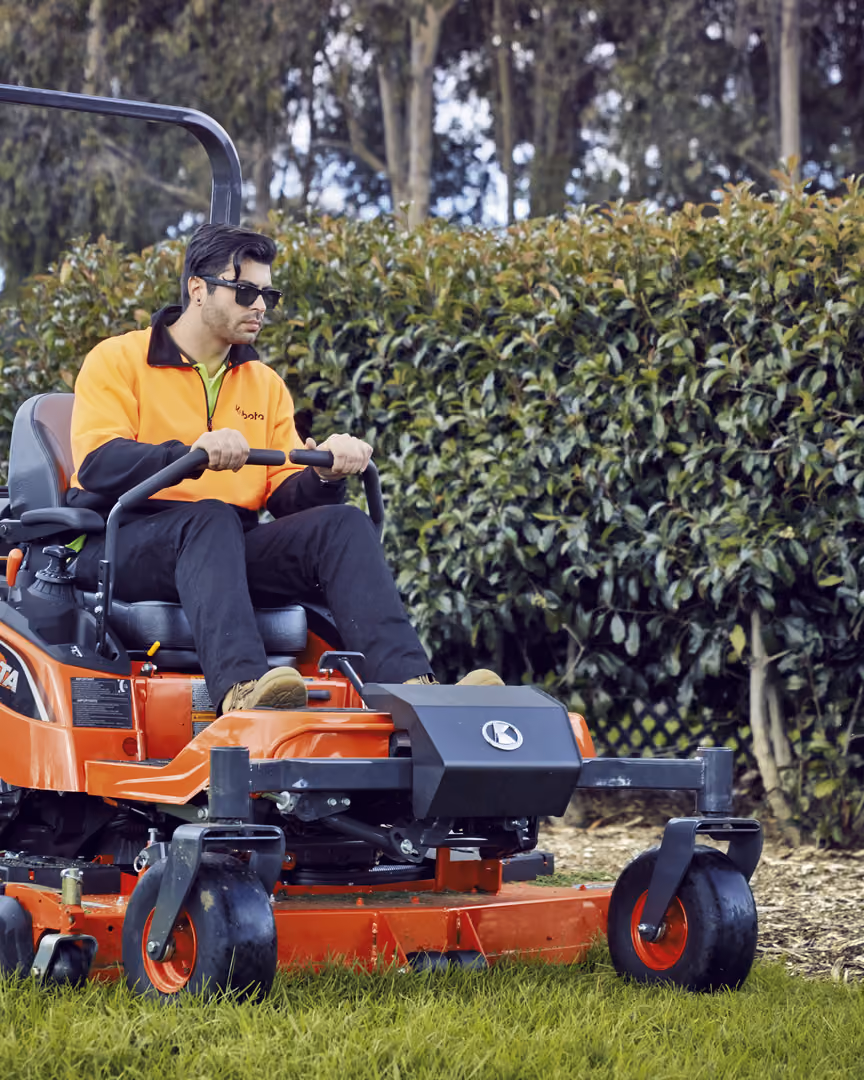 Operator mowing beside a hedge on a Kubota zero-turn mower