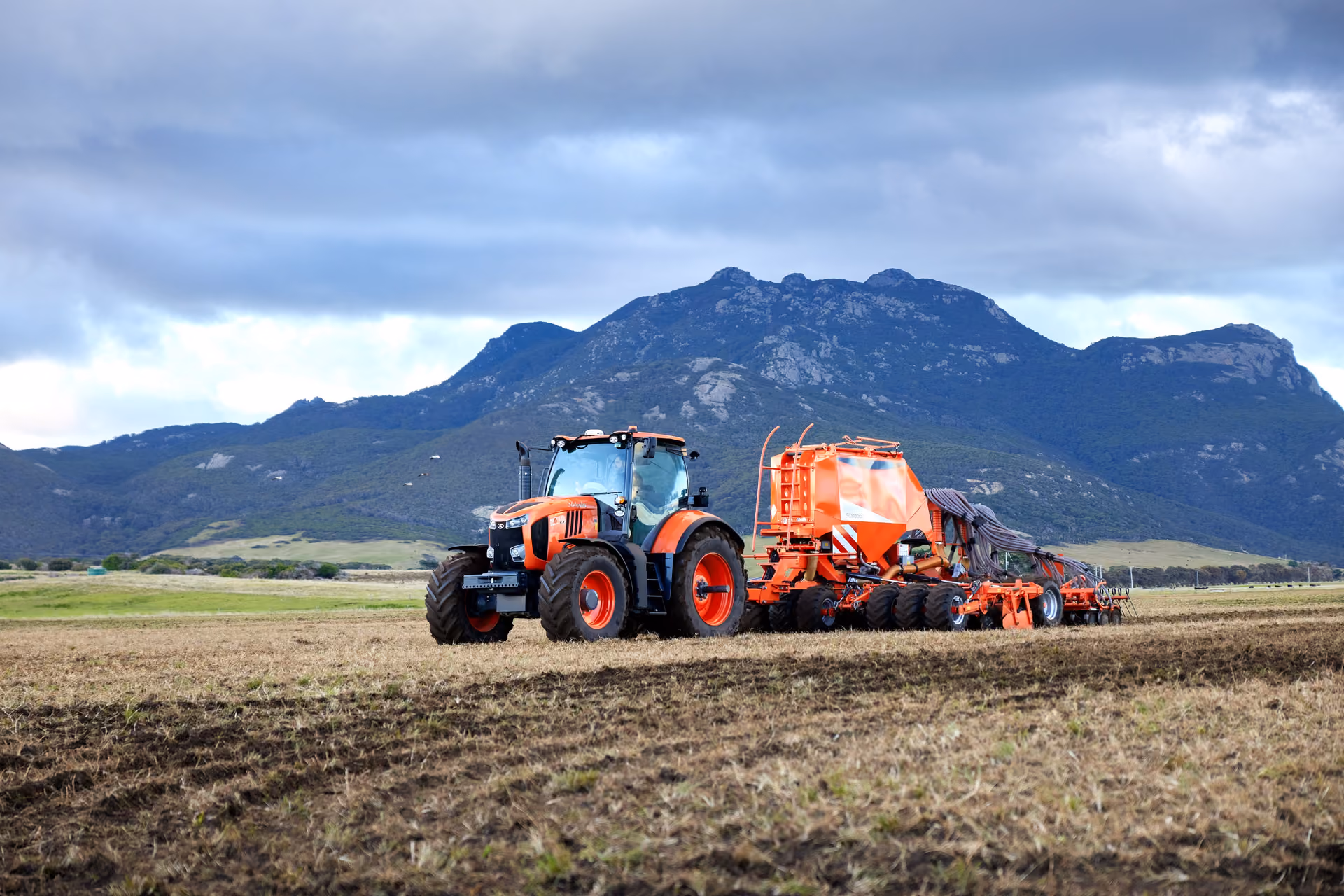 Kubota tractor ploughing a paddock below a mountain range