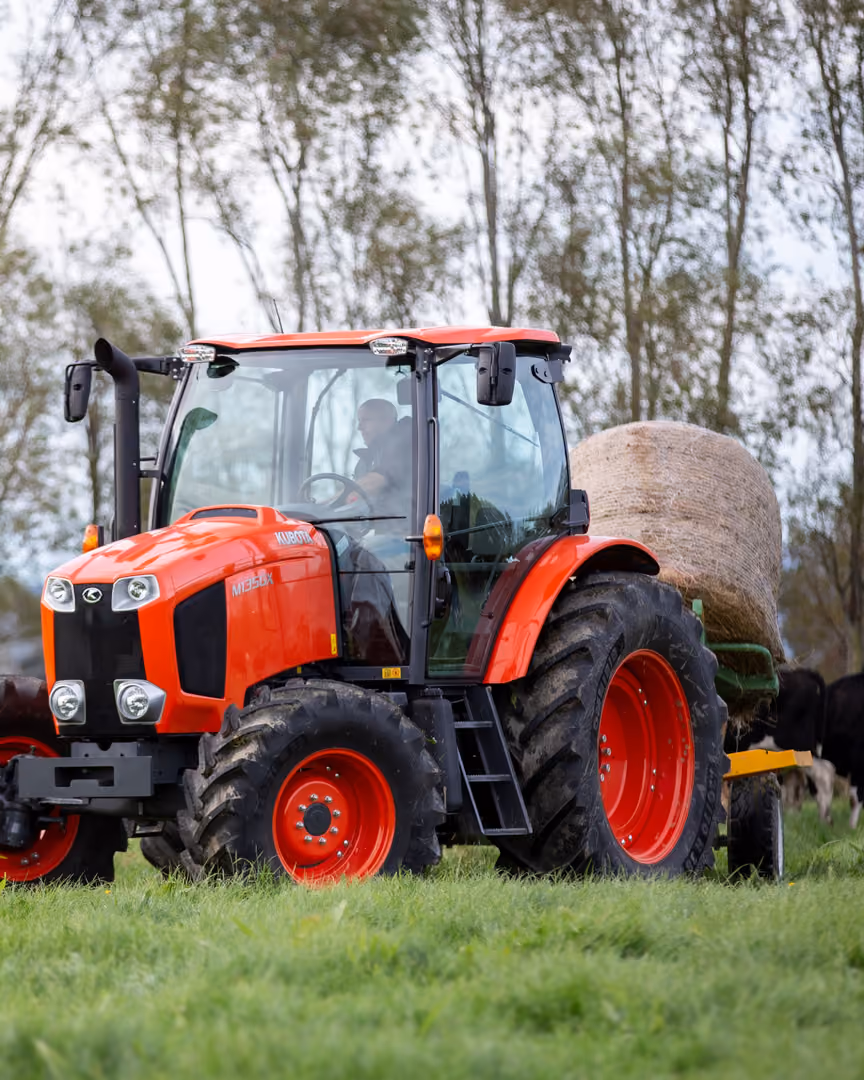 Kubota tractor beside a round hay bale with cattle grazing
