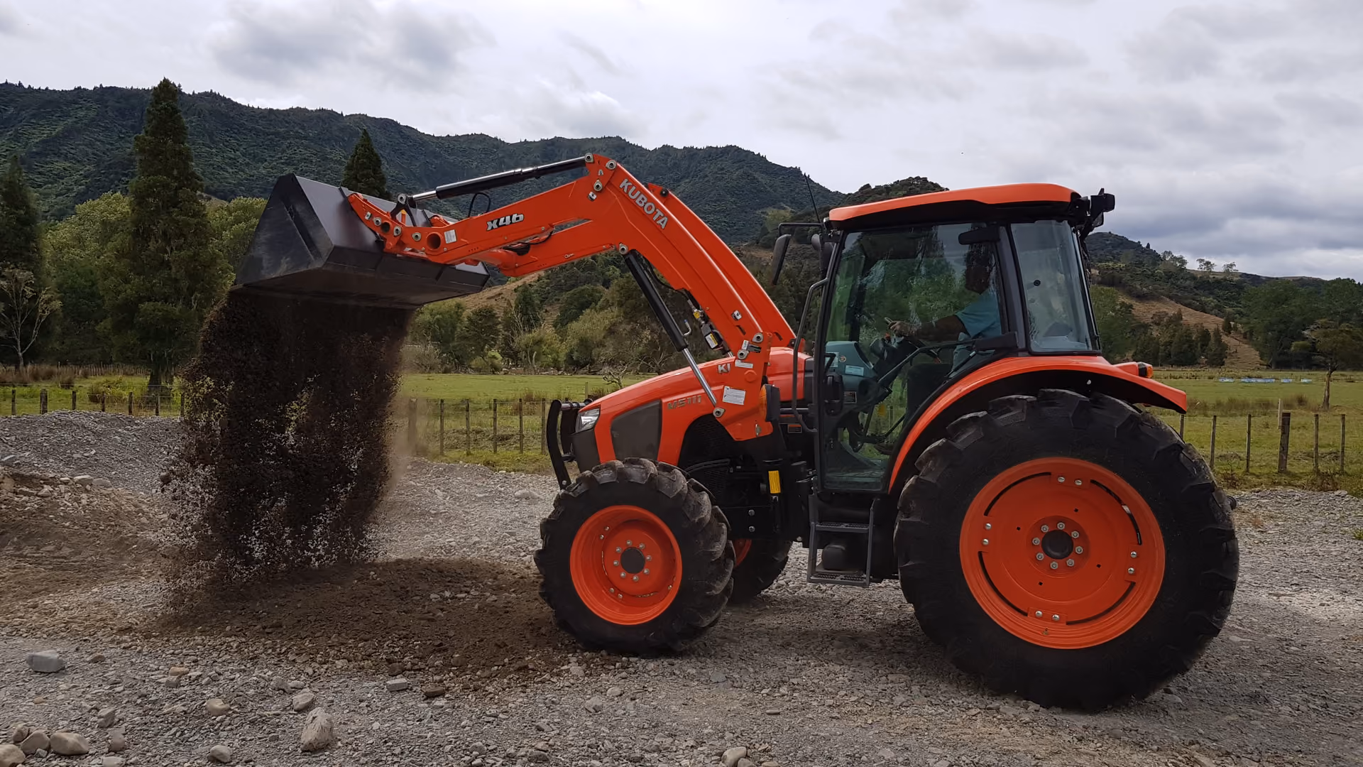 Kubota tractor with front loader working a paddock below rolling hills
