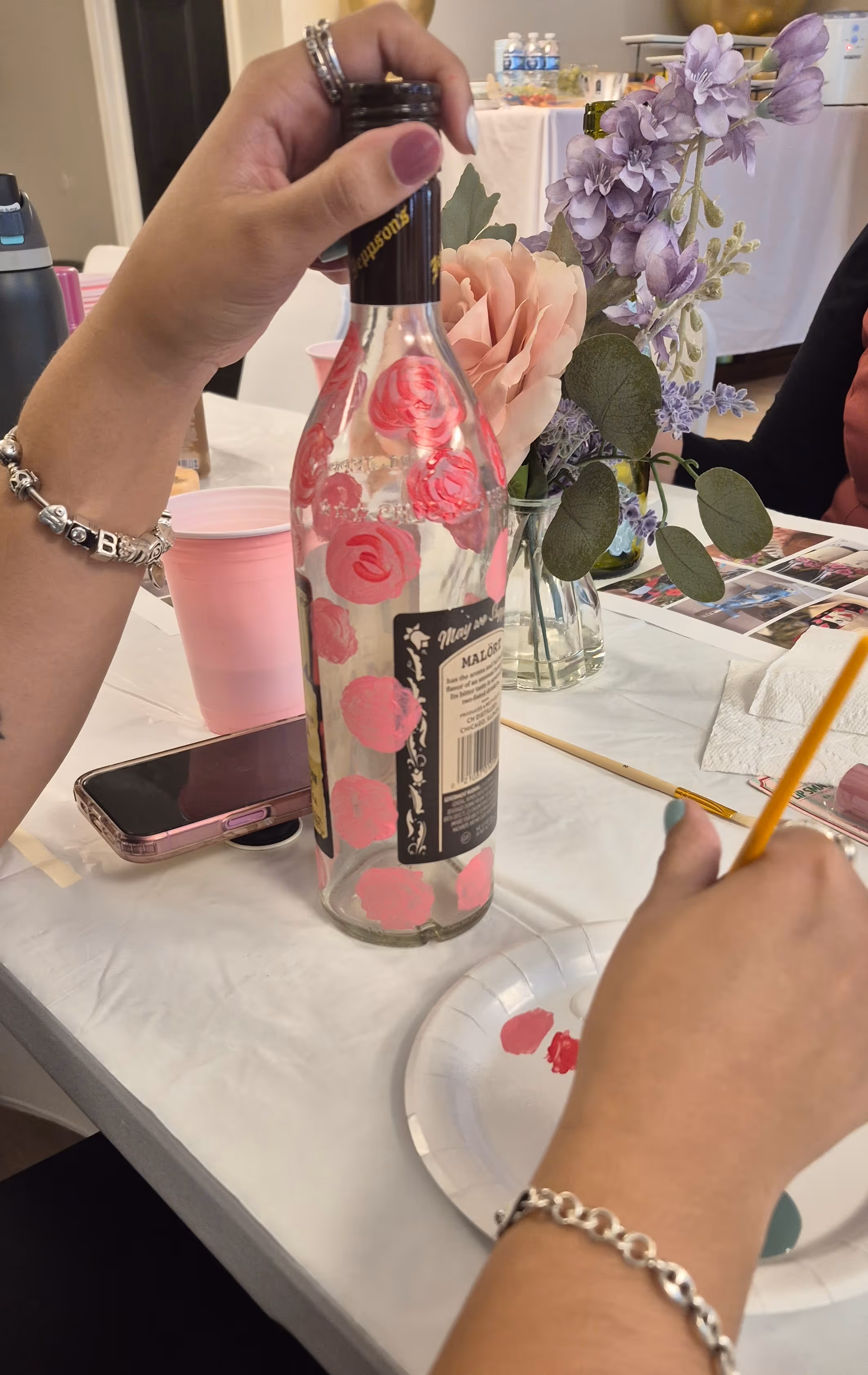 Group of friends wearing party hats clapping and smiling around a woman in a pink dress at her birthday celebration with a cake and desserts.