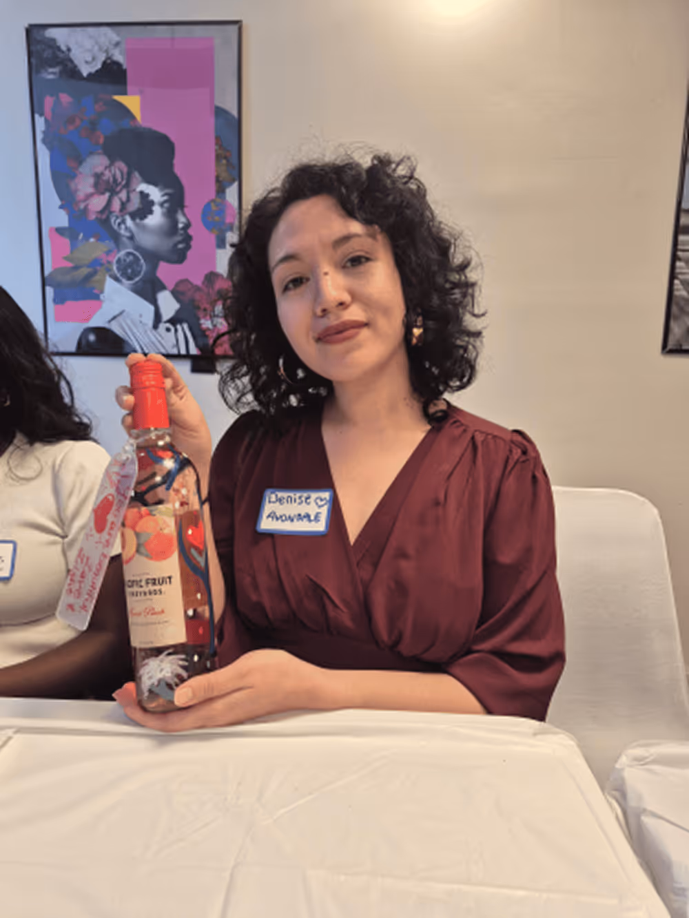 Young woman with straight brown hair holding and presenting four lipsticks in front of a smartphone camera indoors.