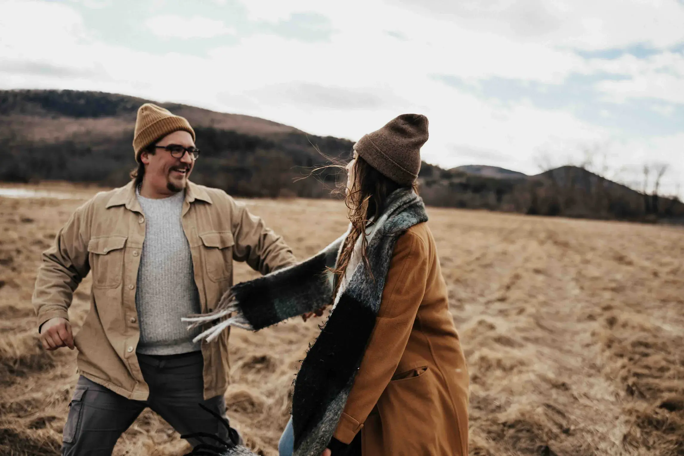 Couple laughing together in an open field during a cozy engagement session in Western Massachusetts, with the Berkshires, Springfield, and Amherst countryside in the background.