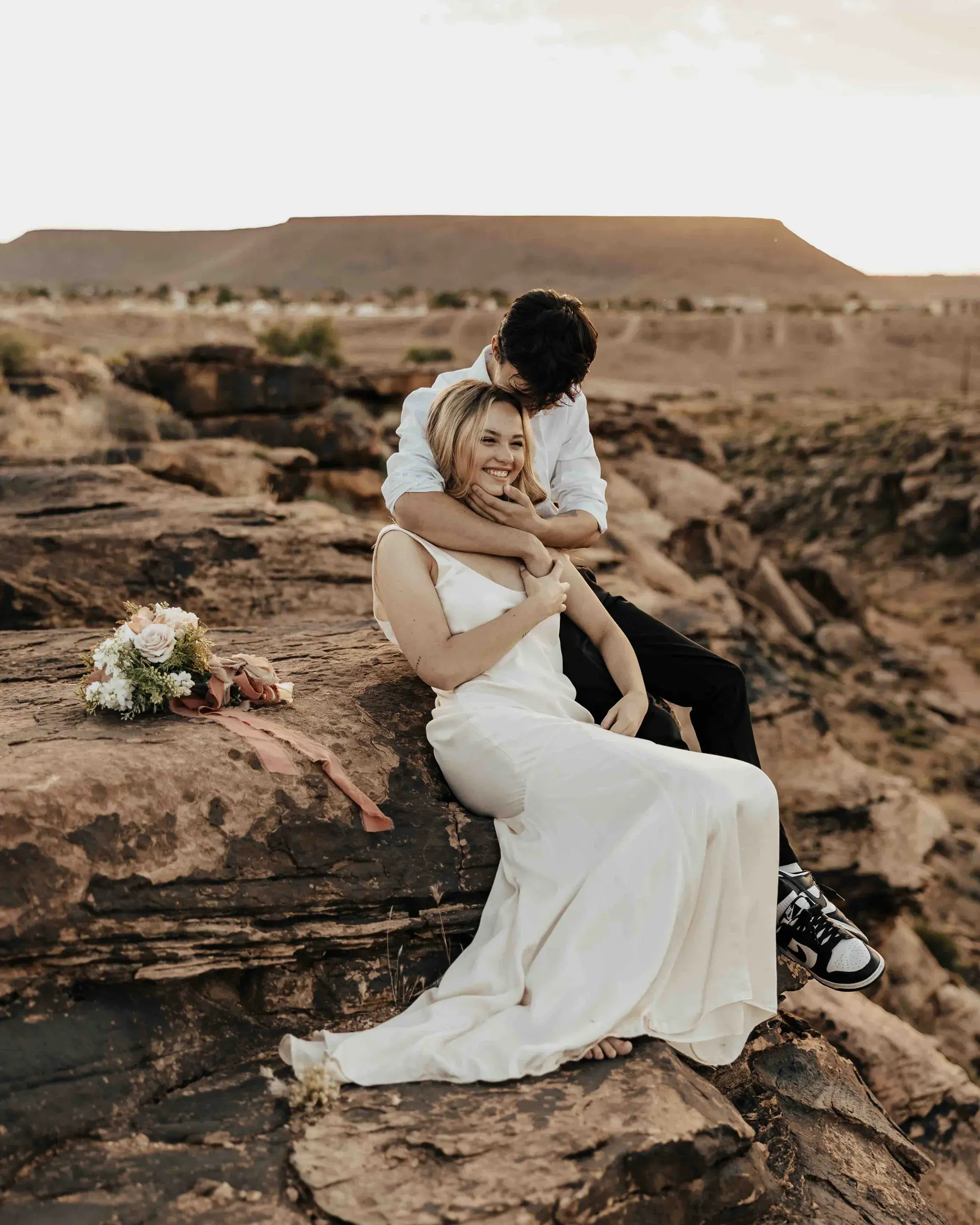 Couple embracing on a rocky mountain landscape during a Utah sunrise elopement, with the bride holding a bouquet beside them.
