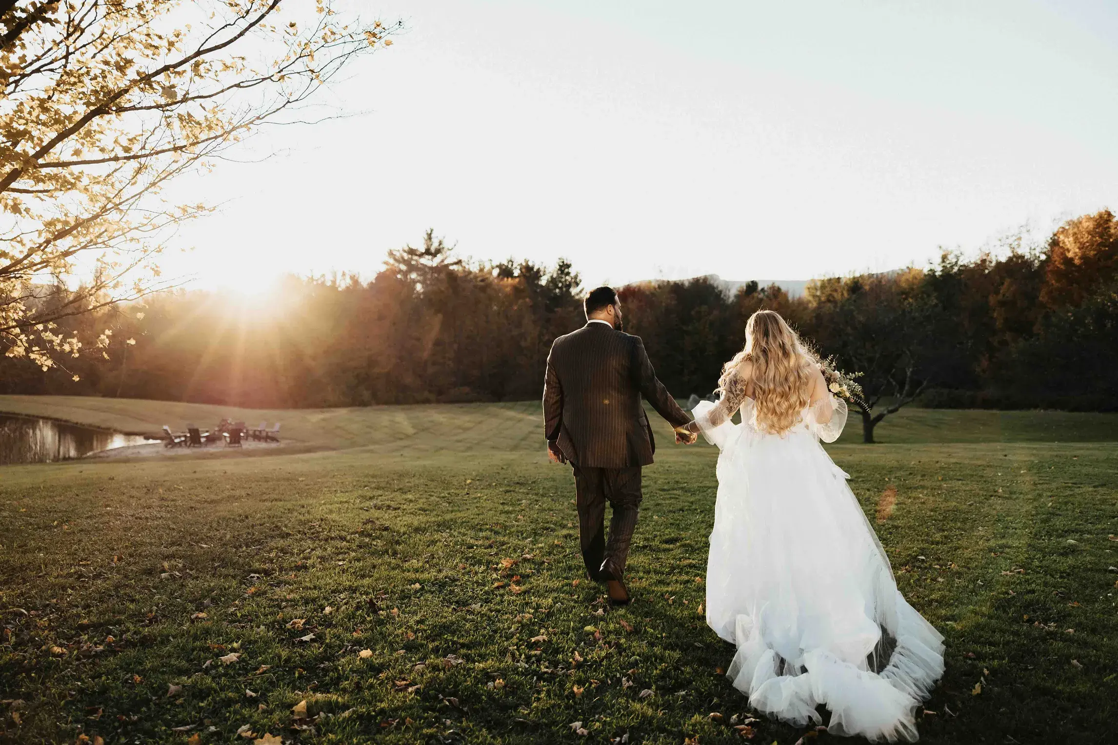 Bride and groom walking hand in hand across the grounds of Meadowstone Manor in Stowe, Vermont, during a romantic sunset wedding portrait.