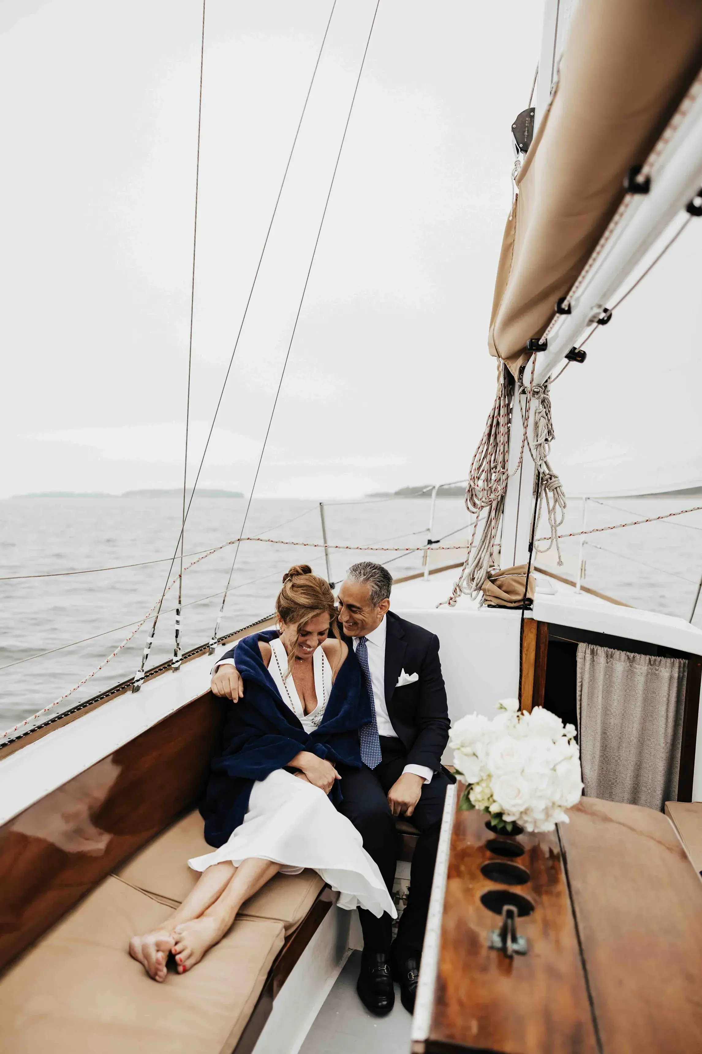 Bride and groom cuddling together aboard a sailboat after their Cape Cod elopement, enjoying a quiet moment surrounded by the ocean and coastal views.