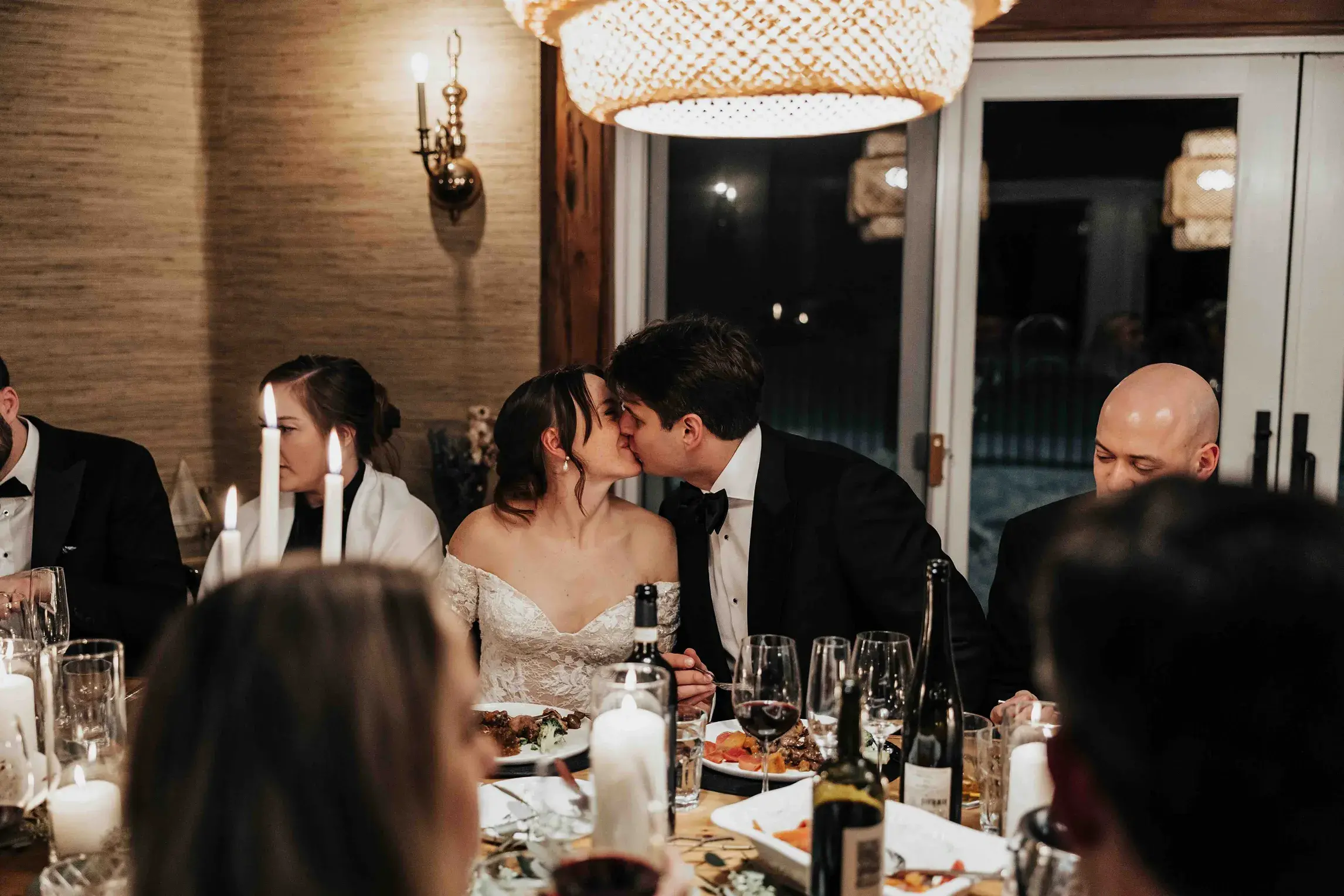 Bride and groom sharing a kiss during their wedding reception dinner at Meadowstone Manor in Stowe, Vermont, surrounded by candlelight and loved ones.