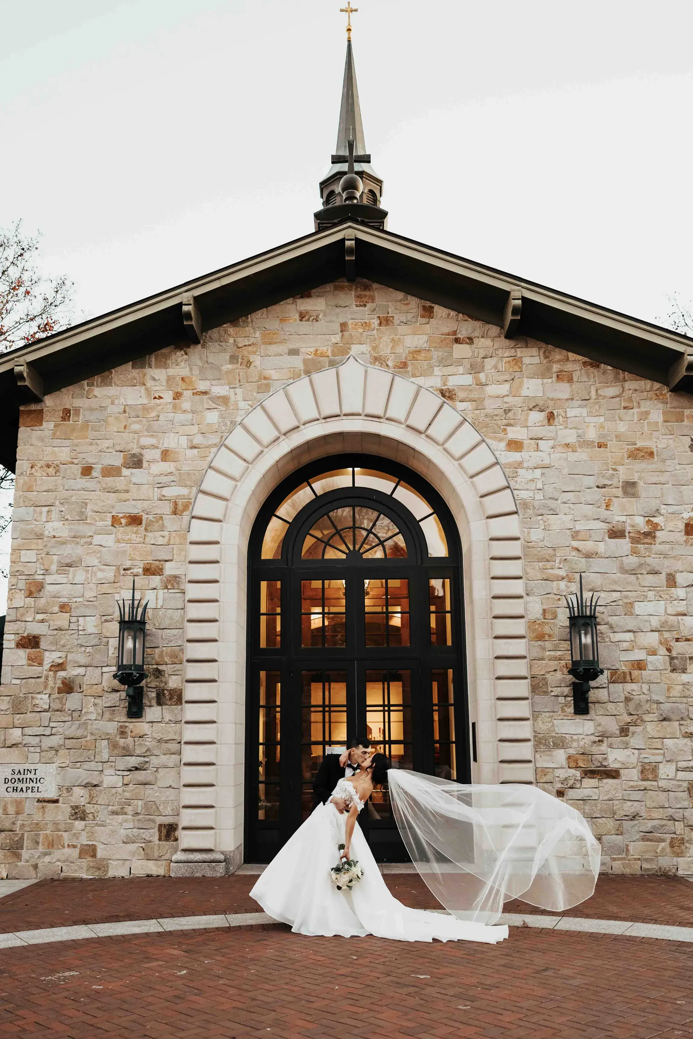Bride and groom sharing a kiss outside Saint Dominic Chapel during their church wedding in Providence, Rhode Island, with the bride's veil flowing in the breeze.