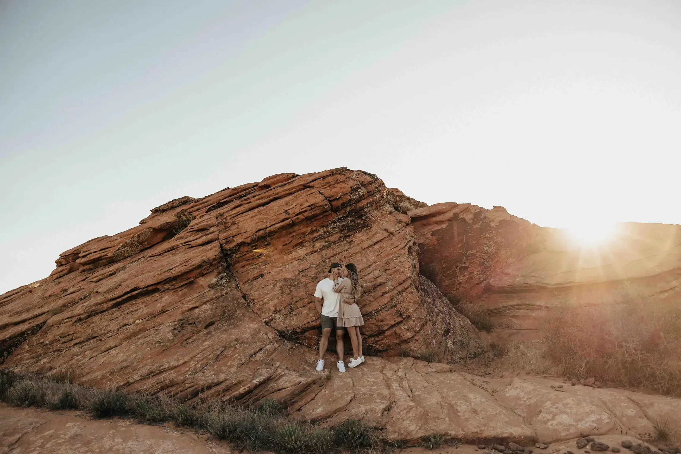Couple embracing beside towering red rock formations during an intimate Utah elopement in a national park, with the golden sunset illuminating the desert landscape.
