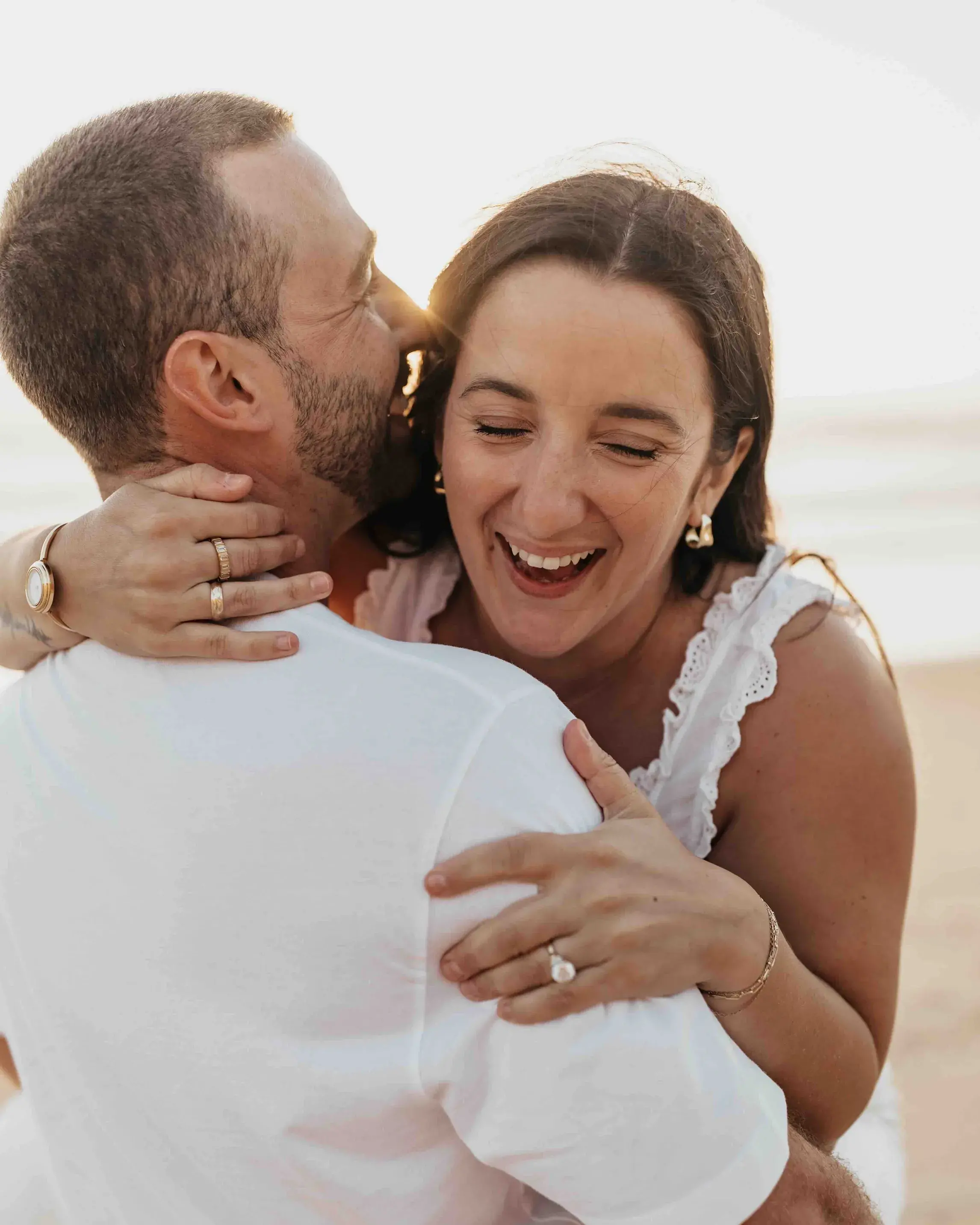 Couple embracing and laughing during a sunset engagement session on the beach in Encinitas, San Diego, with the ocean glowing in the background.