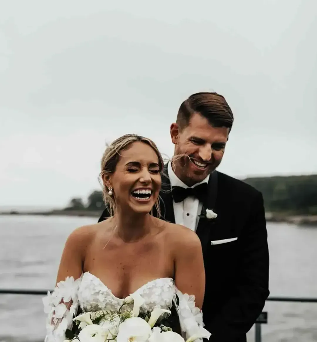 Bride and groom laughing together with a white floral bouquet overlooking the Maine coast and ocean at Stage Neck Inn.