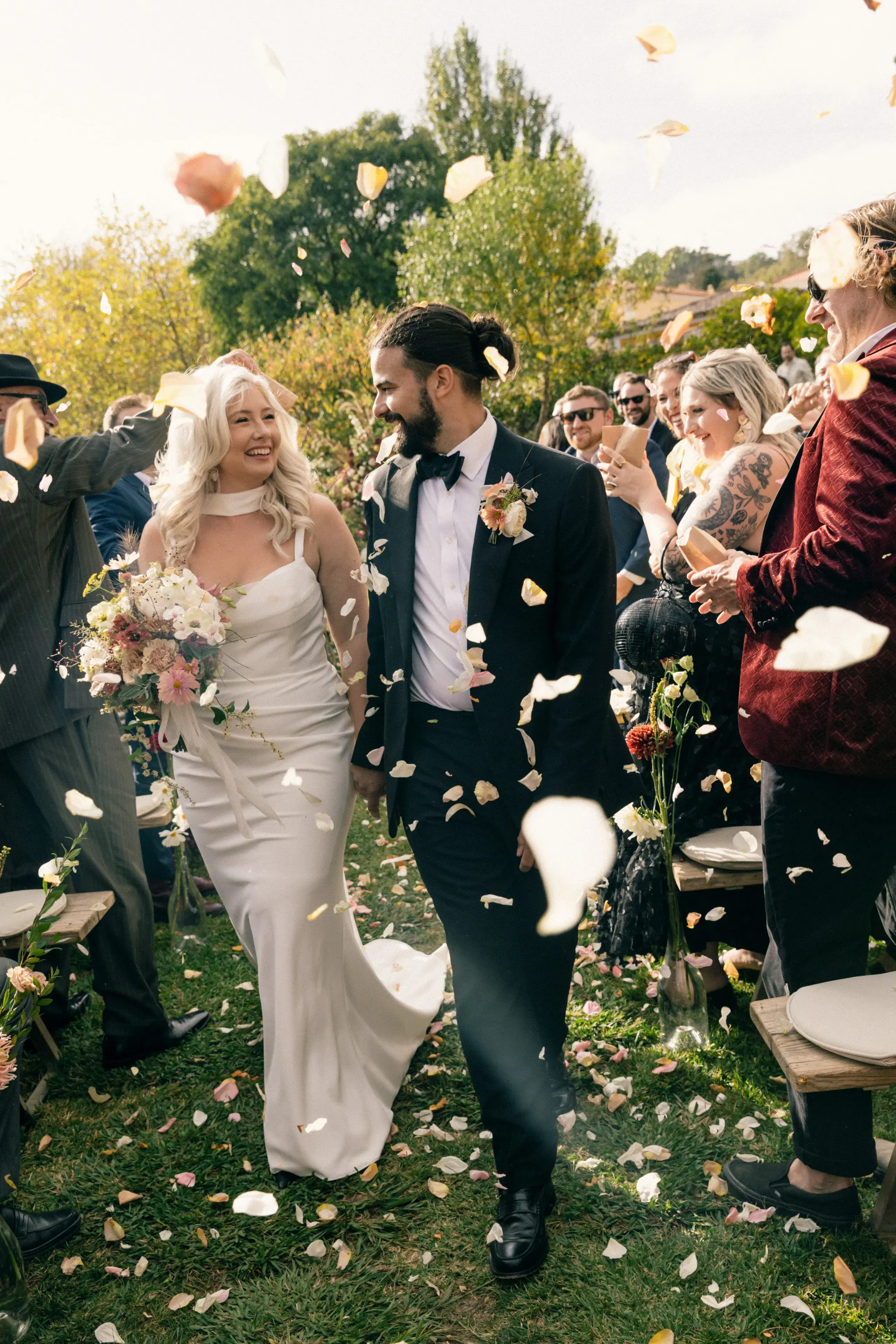 Bride and groom walking hand in hand through flower petals after their outdoor wedding ceremony at a quinta near Mafra, outside Lisbon, Portugal.