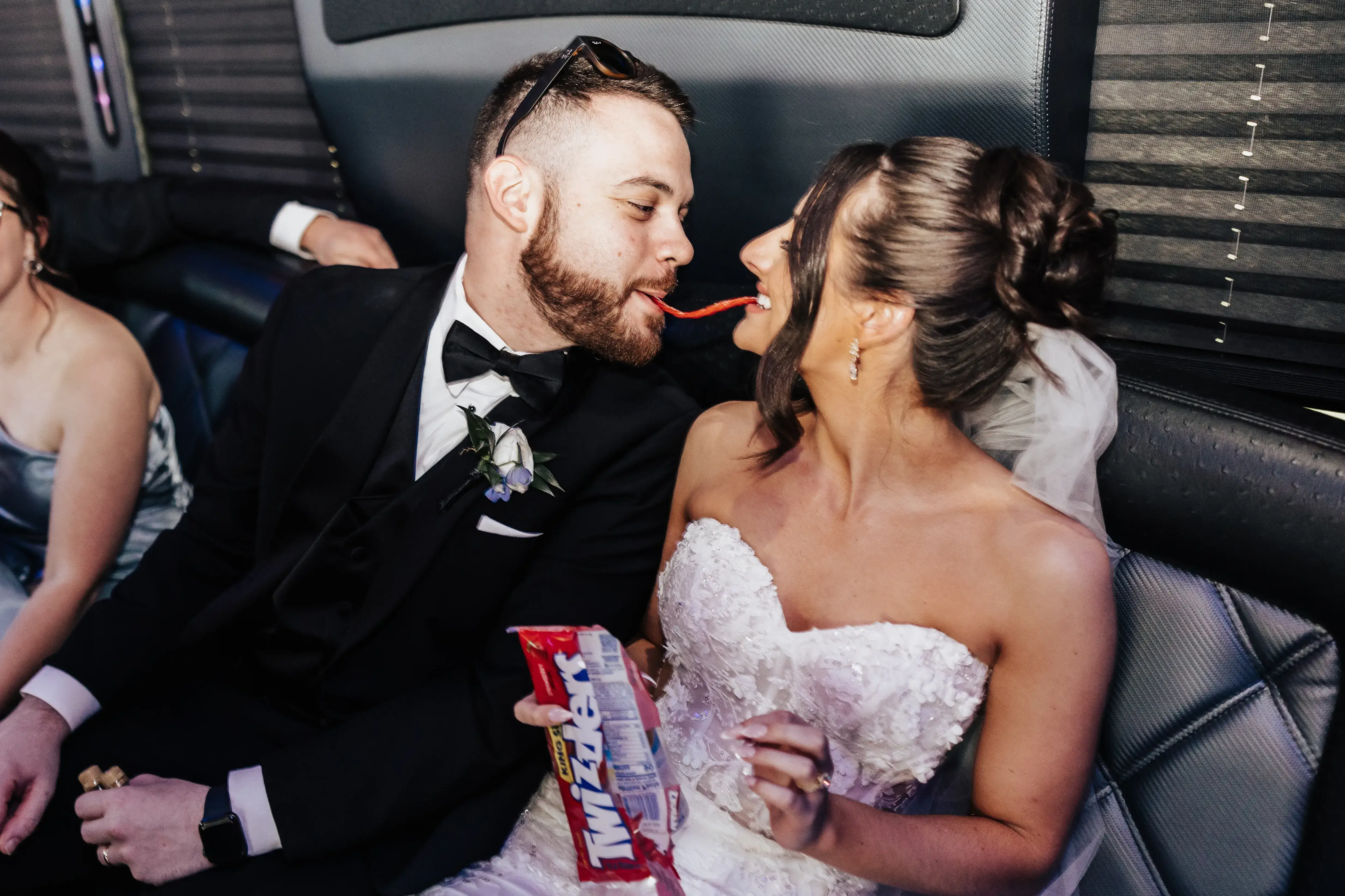 Bride and groom sharing a playful candy moment while seated together in a party bus after their wedding celebration.