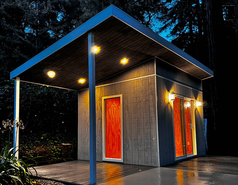 Monterey shed with dark wood siding and bright red-orange doors, located in Boulder Creek, California, photographed at night.