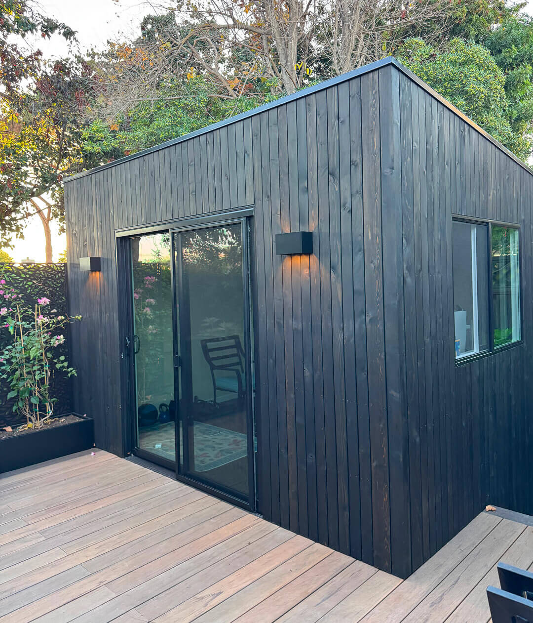 Minima shed backyard studio with dark wood siding, tall glass doors, and a contemporary design on a raised deck in the San Francisco Bay Area, California