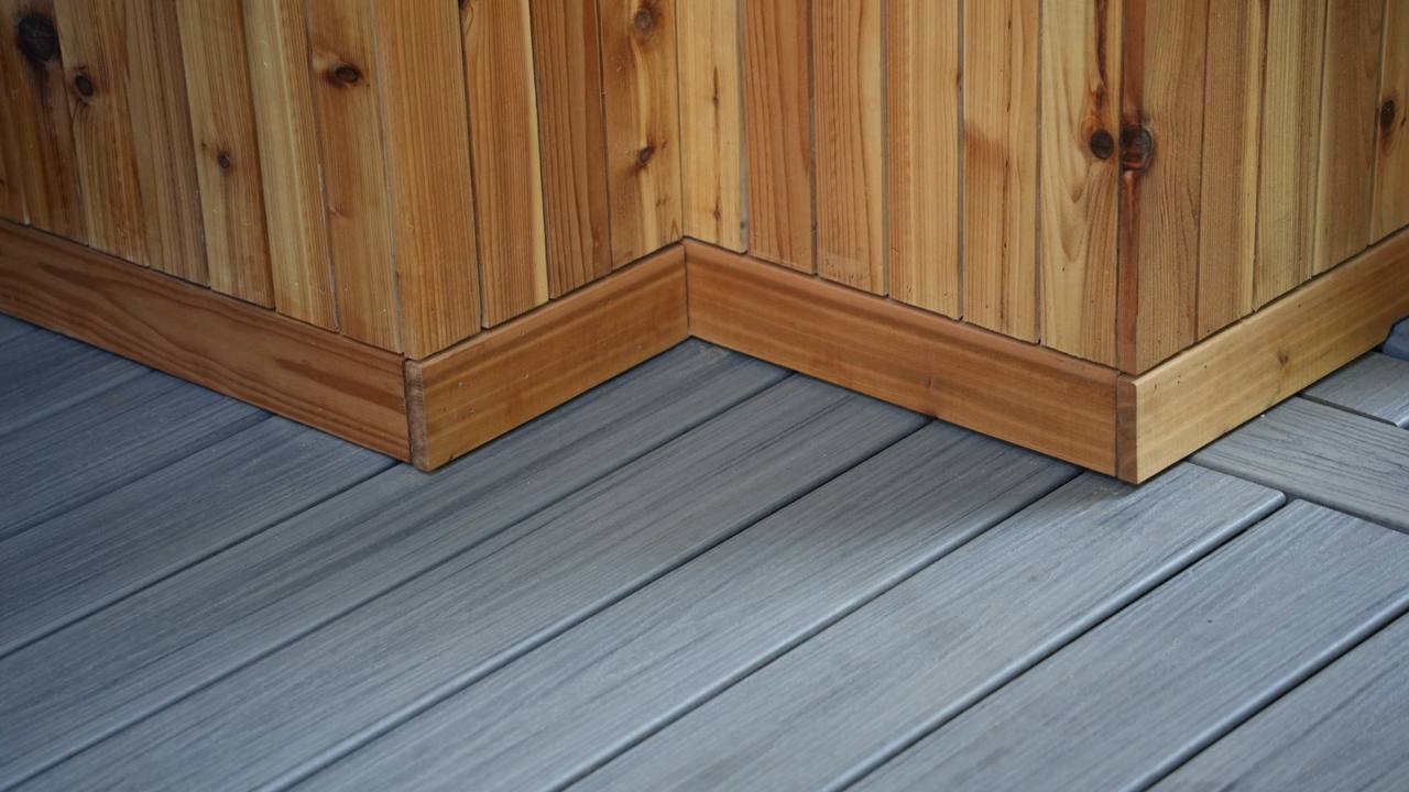 Textured gray composite deck boards meeting a wooden corner base, showcasing durable outdoor patio flooring