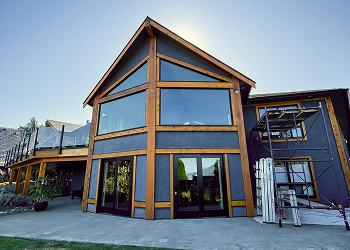Modern house with large glass windows and wooden frame under clear sky at daytime.