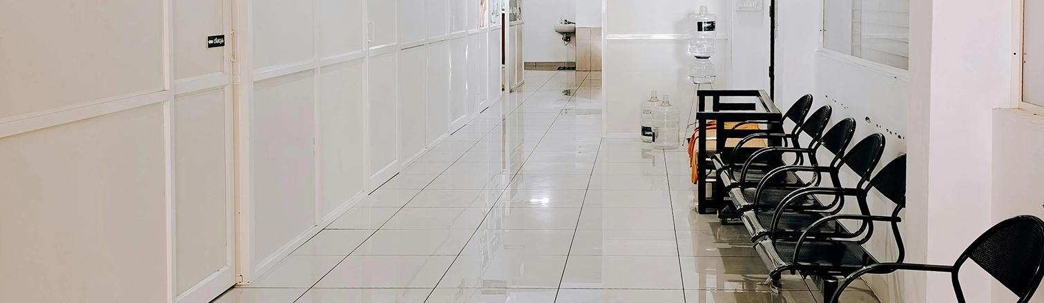 Empty hallway with shiny tiled floor, black metal chairs lined up along a white wall, and water dispensers at the end.