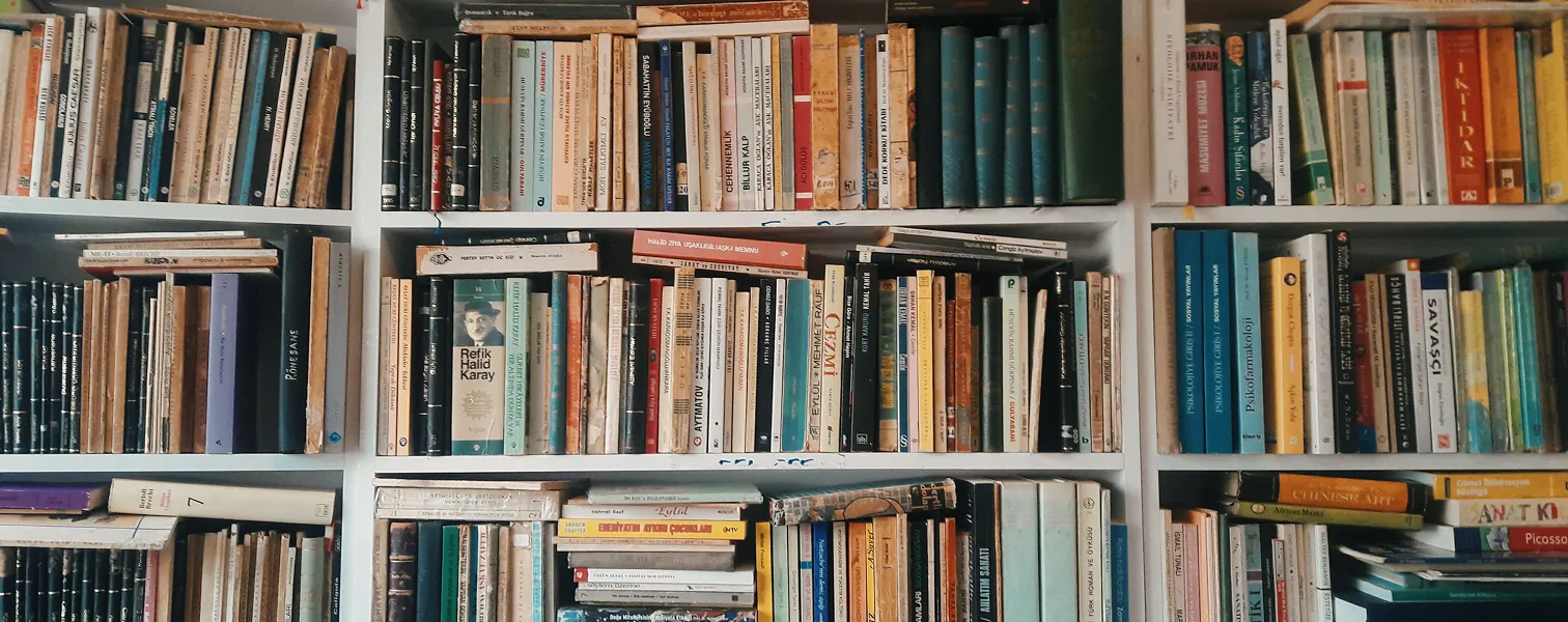 Scaffale pieno di libri di varie dimensioni e colori ordinati in una biblioteca.