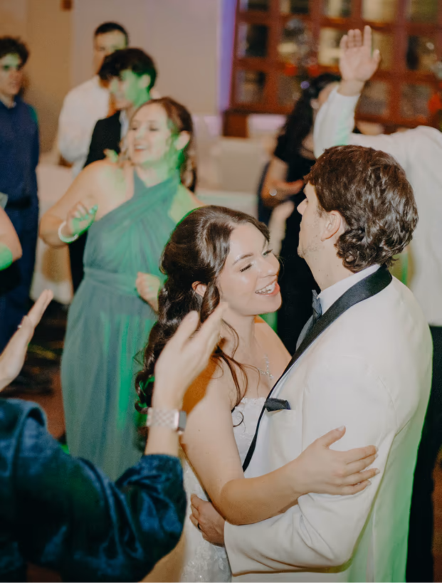 Bride and groom dancing closely at a wedding reception with guests dancing in the background.