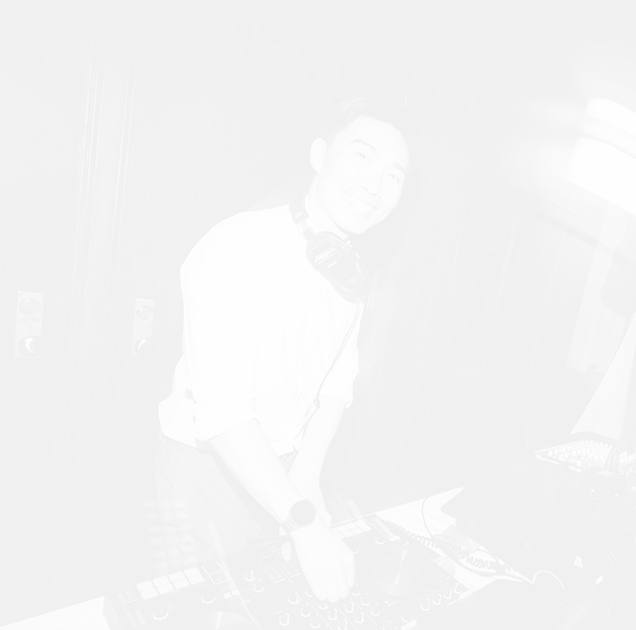 Smiling DJ wearing headphones adjusts controls on a DJ mixer in a dimly lit room.