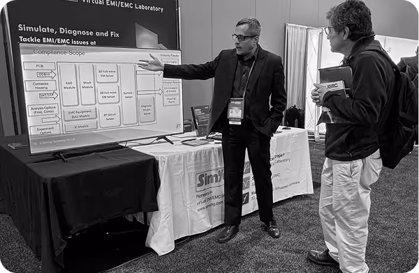 A man in a suit explains a technical poster on EMI/EMC laboratory to another man holding a booklet at a conference.