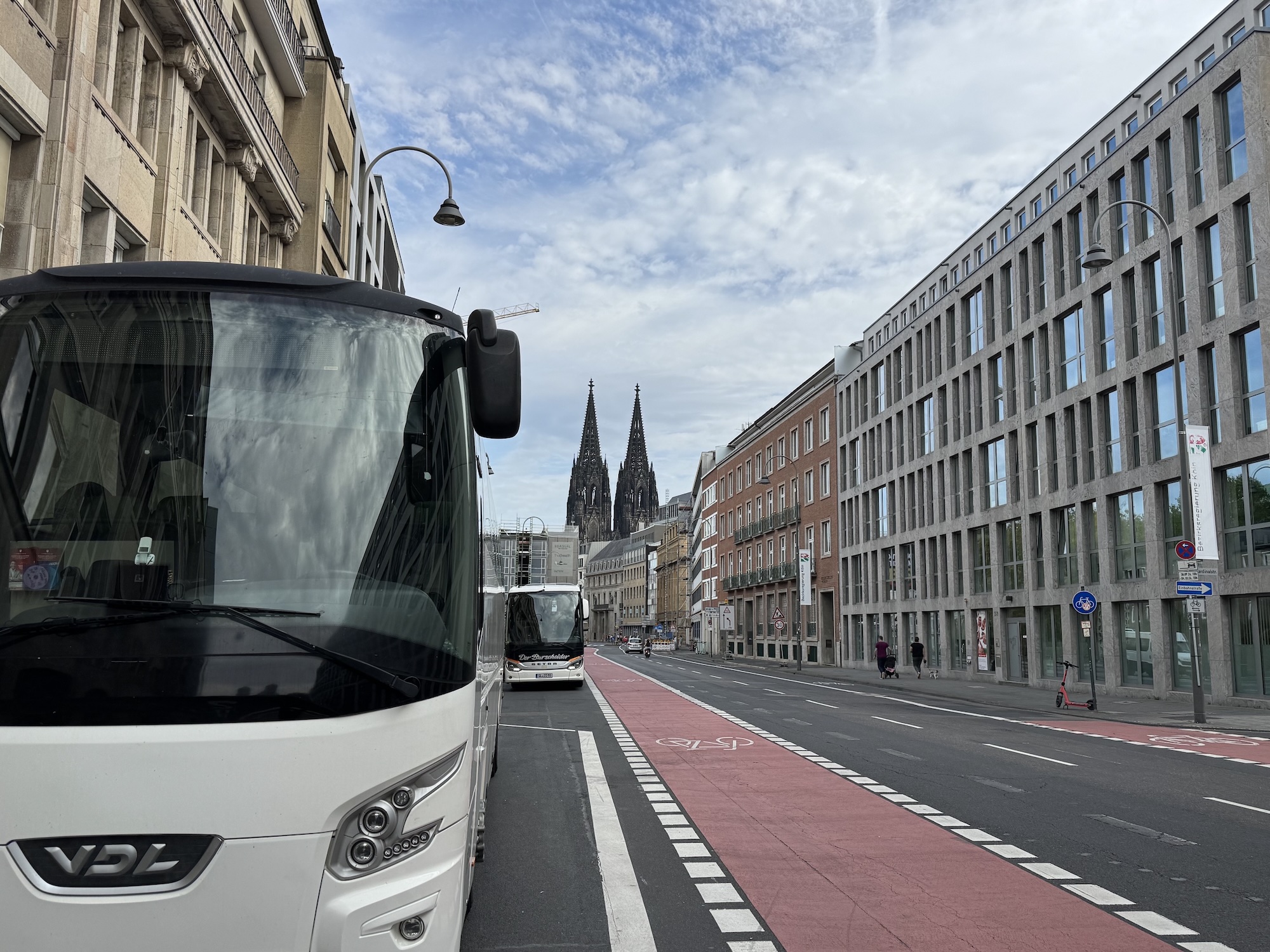 Reisebusse am Haltepunkt Gereonstraße in Köln neben einem rot markierten Radweg, mit den Domtürmen im Hintergrund.