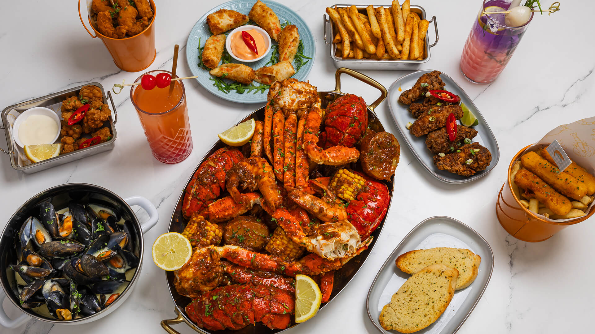 Seafood boil platter with lobster tails, crab legs, shrimp, corn, potatoes, sausage, lemon wedges, and dipping sauce.